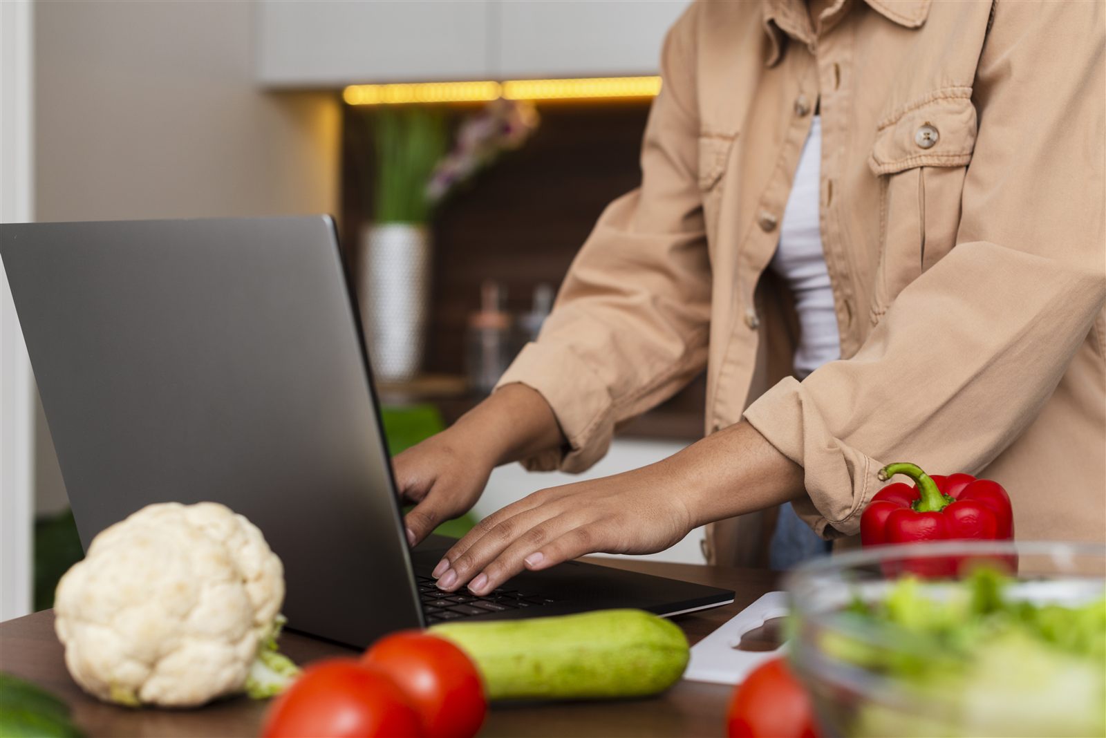Profissional trabalhando no notebook na cozinha, ao lado de legumes frescos
